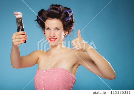woman in hair rollers holds makeup brushes 115386331