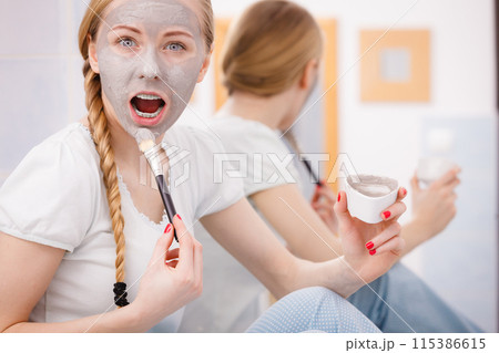 Happy young woman applying mud mask on face Happy young woman applying mud mask on face 115386615