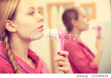 Woman using facial cleansing brush on face 115386634