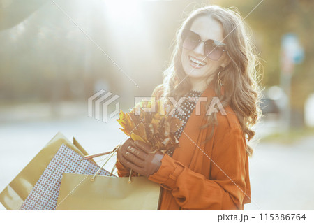 happy modern female in orange trench coat with shopping bags 115386764