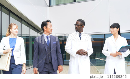 歩きながら会話する多国籍ビジネスパーソンと白衣を着た技術者のグループ 115389243
