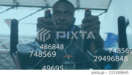 Image of symbols changing over man with face mask exercising on elliptical bike in gym 115389645