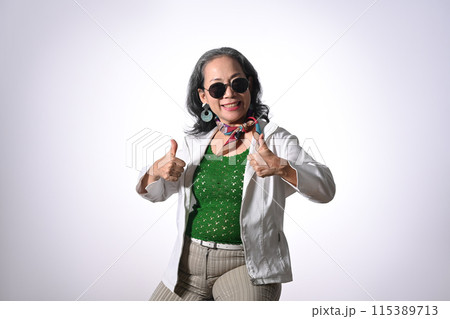 Portrait of cheerful middle aged woman with stylish outfit showing thumbs up over white background 115389713