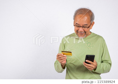Portrait Asian smiling old man is holding a credit card and a cell phone. He is likely checking his bank account balance or making a purchase studio shot isolated on white background 115389924