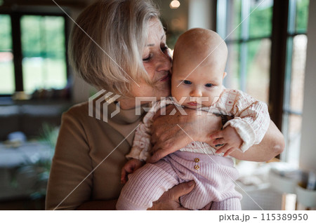 Lovely grandmother holding little baby in arms, looking at her lovingly. Strong bond between grandparent and grandchild. 115389950