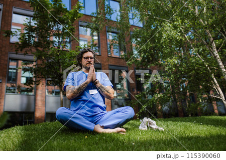 Doctor sitting on grass, meditating and relaxing, winding down from busy workday in hospital. Mental health and life balance for a healthcare worker. 115390060