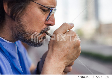 Healthcare worker taking a break, smoking a cigarette outdoors, in front of the hospital building. 115390080