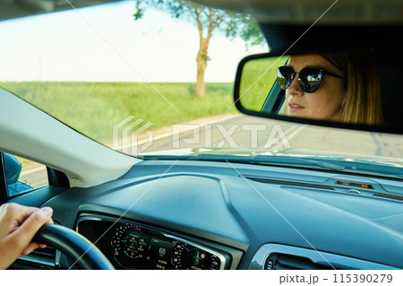 Woman driving car on country road at sunset. Back view of female driver in vehicle with reflection in mirror 115390279
