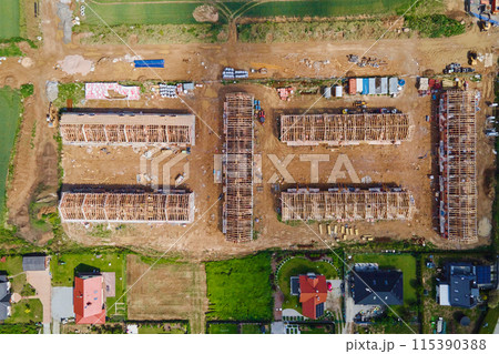 Aerial view of new house construction project in suburban area. Residential building wooden roof frame with truss, post and beams at construction site. Manufacture of new neighborhood in small town 115390388