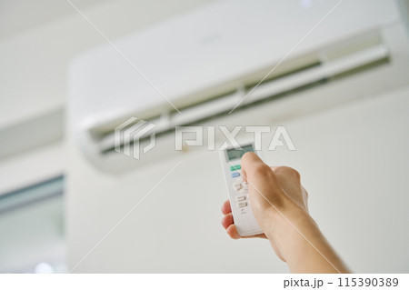 Adjusting air conditioner temperature with remote control. Hand holds remote control and setting comfortable temperature on climate system in apartment 115390389