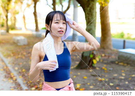 秋の公園の街路樹の道をジョギングする若い女性　ダイエット　ボディメイク　手にタオル　 115390417