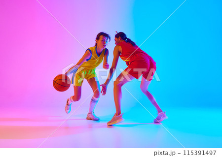 Championship. Two young women, basketball payers in motion with ball, competing against gradient pink blue background in neon light. 115391497