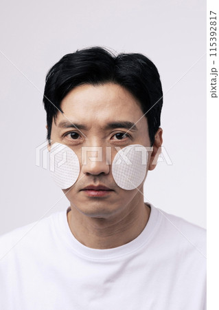 Close up of a middle aged man with a circular cotton pad on both cheeks 115392817