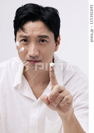 a middle aged man applying cream with his fingers and staring straight ahead a middle aged man applying cream with his fingers and staring straight ahead 115392845