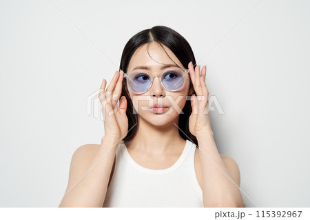 Asian woman staring in one spot wearing transparent sunglasses with both hands 115392967