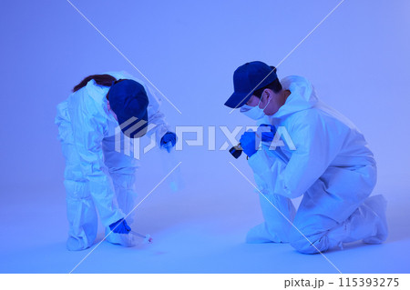 CSI Scientific Investigation Unit male and female researchers identifying and collecting evidence at crime and incident sites with blue lights 115393275