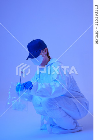 CSI female researcher sitting at crime and incident sites with blue lights collecting evidence in envelopes 115393313