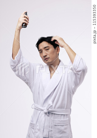 a middle aged man holding a spray bottle and spraying mist on his head a middle aged man holding a spray bottle and spraying mist on his head 115393350