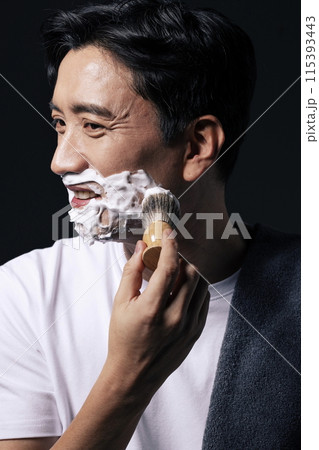 a middle aged man who foams his face with a shaving brush 115393443