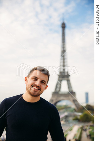 Cheerful man tourist in dark blue pullover is standing on the background of the Eiffel Tower 115393804