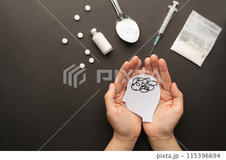 Drug addiction induced psychosis. Hands holding human brain feeling confused symbol with drug powder, syringe and pills on dark background. International Day against Drug Abuse. Drug addiction induced psychosis. Hands holding human brain feeling confused symbol with drug powder, syringe and pills on dark background. International Day against Drug Abuse. 115396694