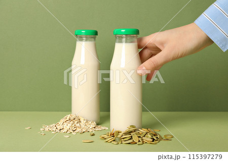 Bottles of milk, hand, oatmeal and pumpkin seeds on green background 115397279
