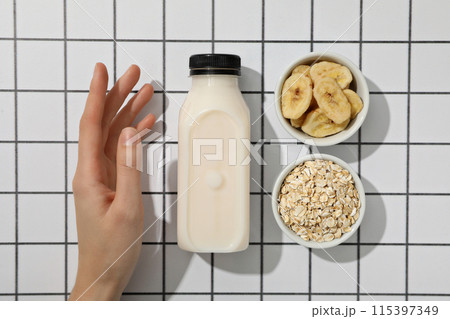 Bottle with milk, hand and bowls with oatmeal and sliced bananas on light background, top view 115397349