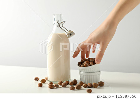 Bottle with milk, hand and bowls with nuts on white background Bottle with milk, hand and bowls with nuts on white background 115397350