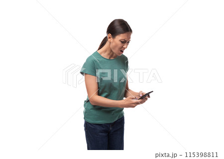 surprised young brunette woman dressed in green t-shirt and jeans uses smartphone 115398811