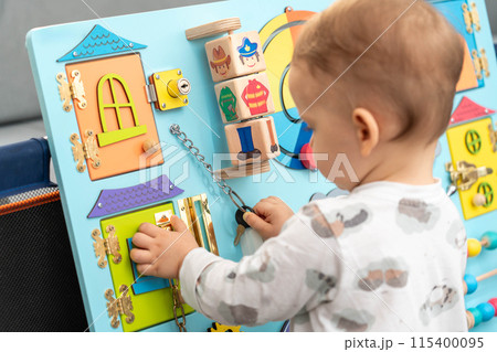 A toddler uses a key for a small lock while playing with a busy board 115400095