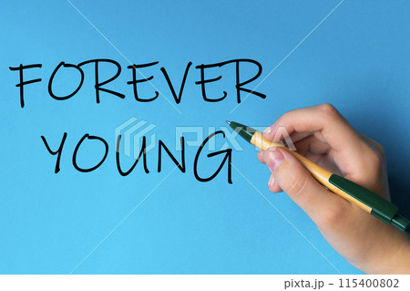 Children hand with pen write on an blue white background. Writing hand. Word Forever young Children hand with pen write on an blue white background. Writing hand. Word Forever young 115400802