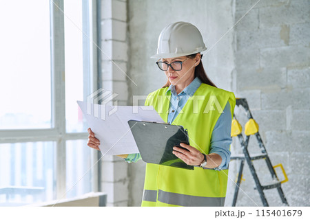 Technical profession woman in protective vest helmet working on construction 115401679