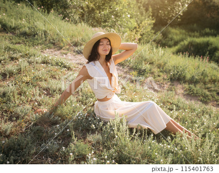 Woman Relaxing in Sunny Meadow Wearing Stylish Summer Hat and White Outfit 115401763