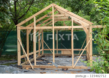 Construction of a large wood greenhouse in garden. Wooden domestic greenhouse for growing vegetables or flowers. 115402712