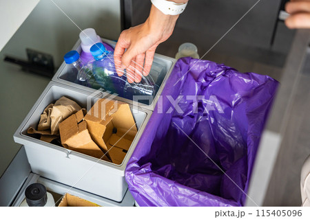 Hand of woman throwing trash into household bins for waste sorting in the kitchen for recycle. Plastic, paper, bio and mixed waste. Sorting waste at home concept 115405096