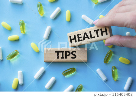 Health Tips symbol. Wooden blocks with words Health Tips. Beautiful blue background with pills. Doctor hand. Medicine and Health Tips concept. Copy space. 115405408