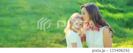 Happy cheerful smiling mother with little girl child daughter on the grass in sunny summer park 115406292