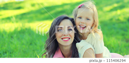 Happy cheerful smiling mother with little girl child daughter on the grass in sunny summer park 115406294