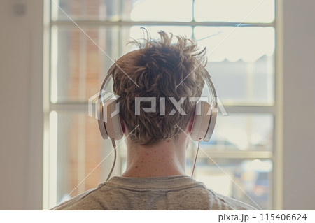 Man wearing headphones, listening to music in front of a window 115406624