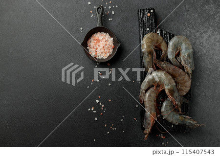 Large king prawns raw on a black cutting board. Hot pepper, salt. Black background 115407543