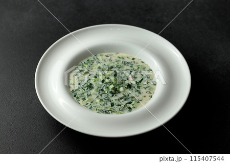 Cold soup with fresh cucumbers, sausage, broth and sour cream in a plate-hat on a black background. A traditional dish is okroshka Cold soup with fresh cucumbers, sausage, broth and sour cream in a plate-hat on a black background. A traditional dish is okroshka 115407544
