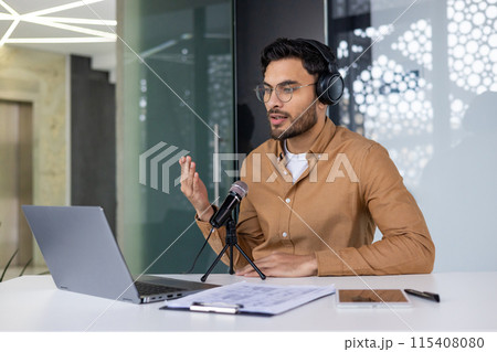 Young professional wearing headphones and recording podcast in a modern office. Using a laptop and microphone for content creation. Young professional wearing headphones and recording podcast in a modern office. Using a laptop and microphone for content creation. 115408080