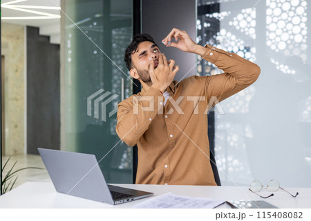 Man using eye drops while working at the office with laptop. Workplace discomfort and eye care. 115408082