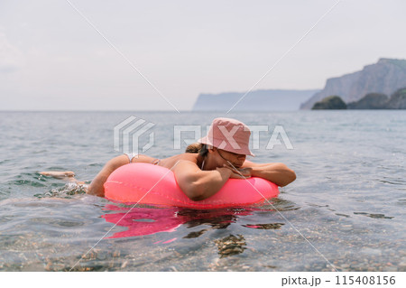 A woman is laying on a pink inflatable raft in the ocean. The scene is peaceful and relaxing, with the woman enjoying the water and the sun. 115408156