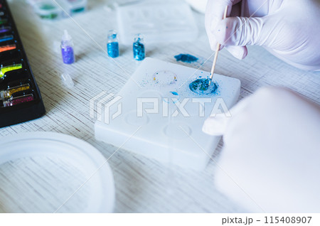 Children's hands in gloves fill an epoxy resin ring mold with decorative sparkles Children's hands in gloves fill an epoxy resin ring mold with decorative sparkles 115408907