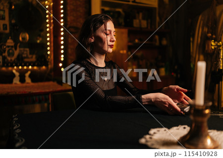 Mysterious fortuneteller dealing Tarot cards before forecasting future for client. Female fortune-telling having divination session with tarot cards at dark esoteric room. Concept of divination, magic 115410928