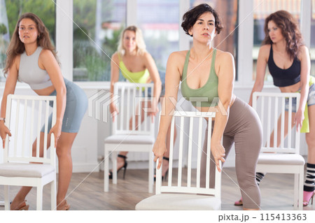 Active female dancer with group of women of different ages practicing strip plastic movements near chair in training hall during dancing classes Active female dancer with group of women of different ages practicing strip plastic movements near chair in training hall during dancing classes 115413363
