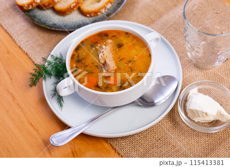 Popular dish of Russian cuisine is pickle soup with meat, cooked on basis of pickled cucumbers and pearl barley or rice, decorated with sprig of parsley 115413381