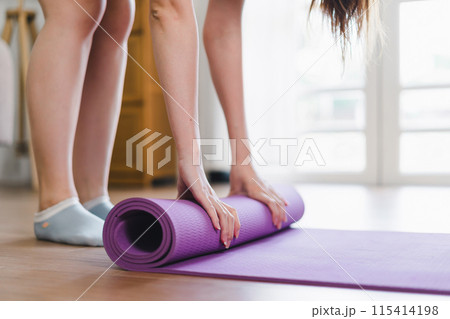 Woman rolling exercise mat in living room. Yoga at home active lifestyle concept Woman rolling exercise mat in living room. Yoga at home active lifestyle concept 115414198