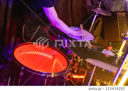 Drummer playing drums at rock concert, music performance with drum kit and cymbals in background 115414283
